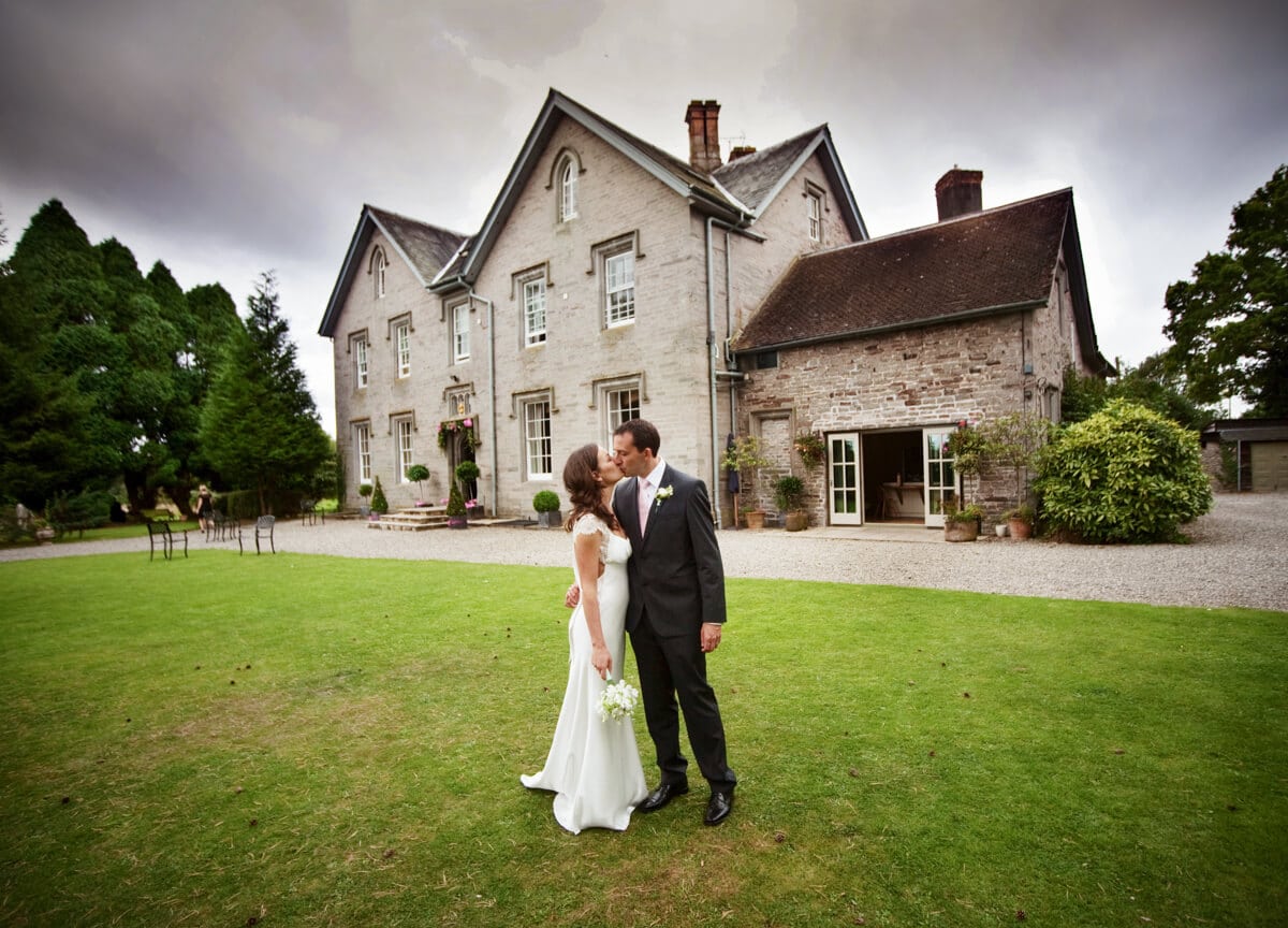 Bride and groom kissing in front of Lemore Manor in Herefordshire