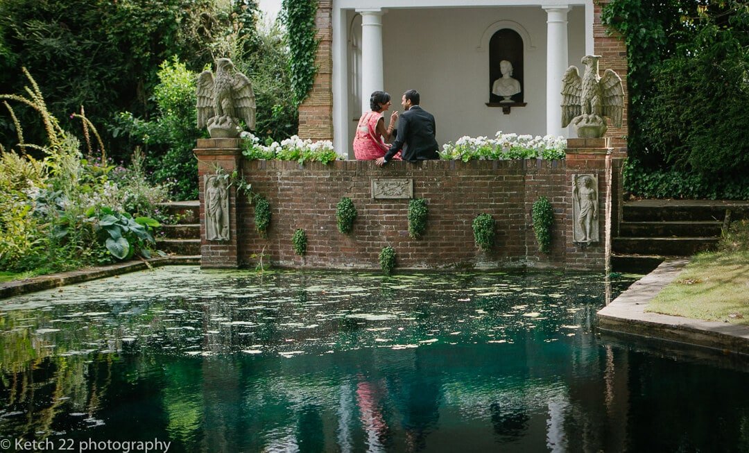 Indian bride and groom sitting in water garden at London wedding venue