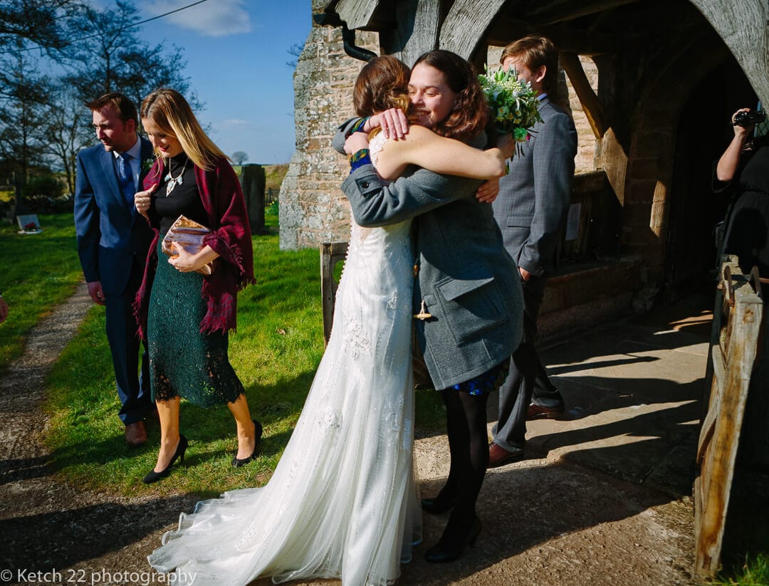 Bride hugging friend outside church at Herefordshire wedding