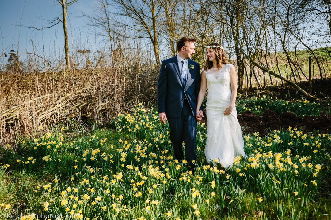 Bride and groom walking amongst daffodils at spring wedding at Dewsall Court