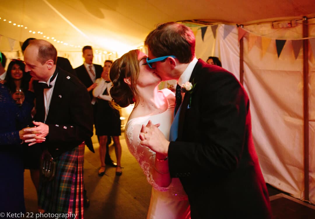 Groom with blue sunglasses kissing bride during first dance