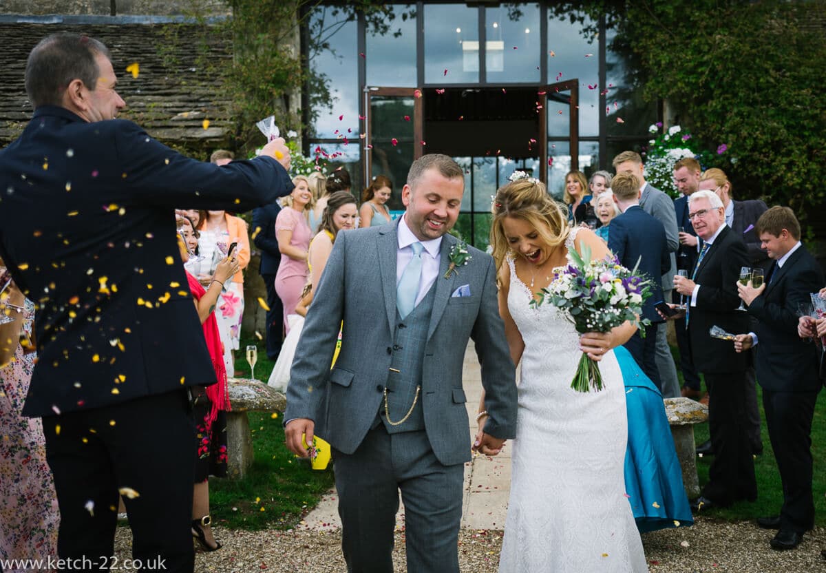 bride and groom walk through confetti at Gloucestershire wedding