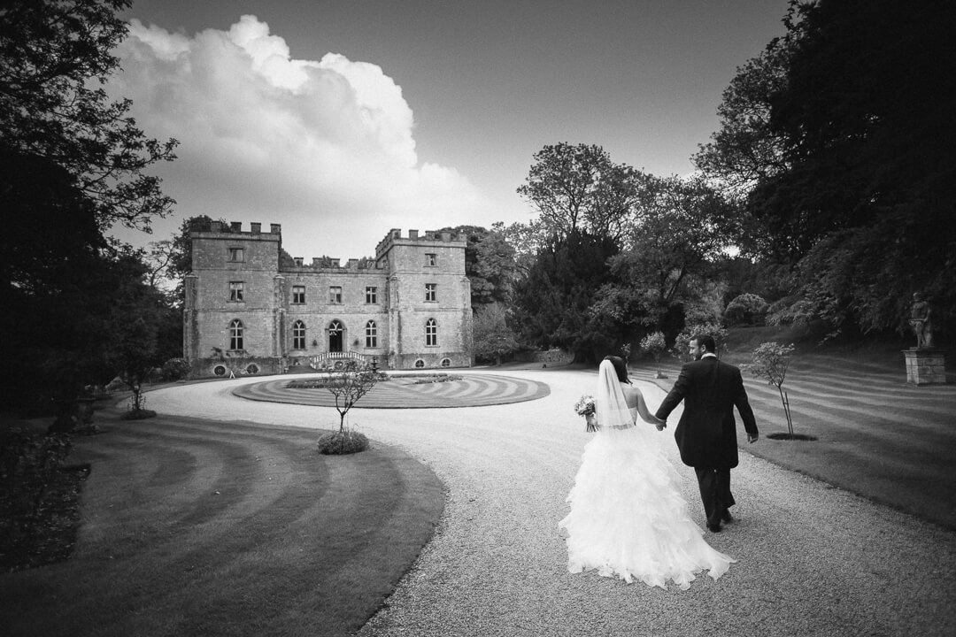 Bride and groom walking in in front of Clearwell Castle wedding venue in Gloucestershire