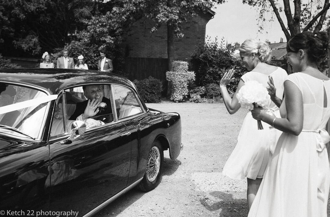 Groom waving goodbye from black wedding car