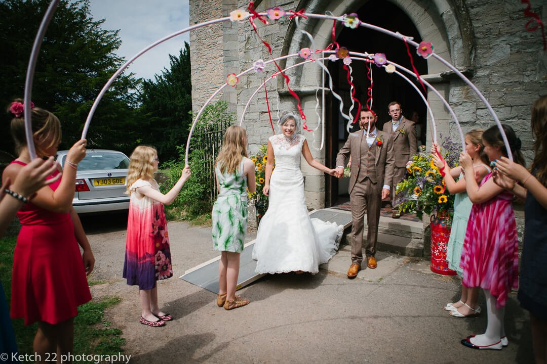Bride and groom walking through colourful arch hoops after wedding ceremony