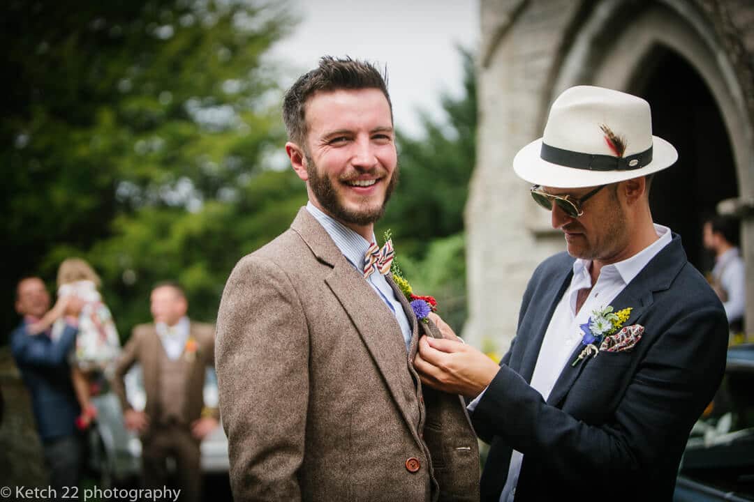 Best man buttons flower on grooms jacket at rural wedding