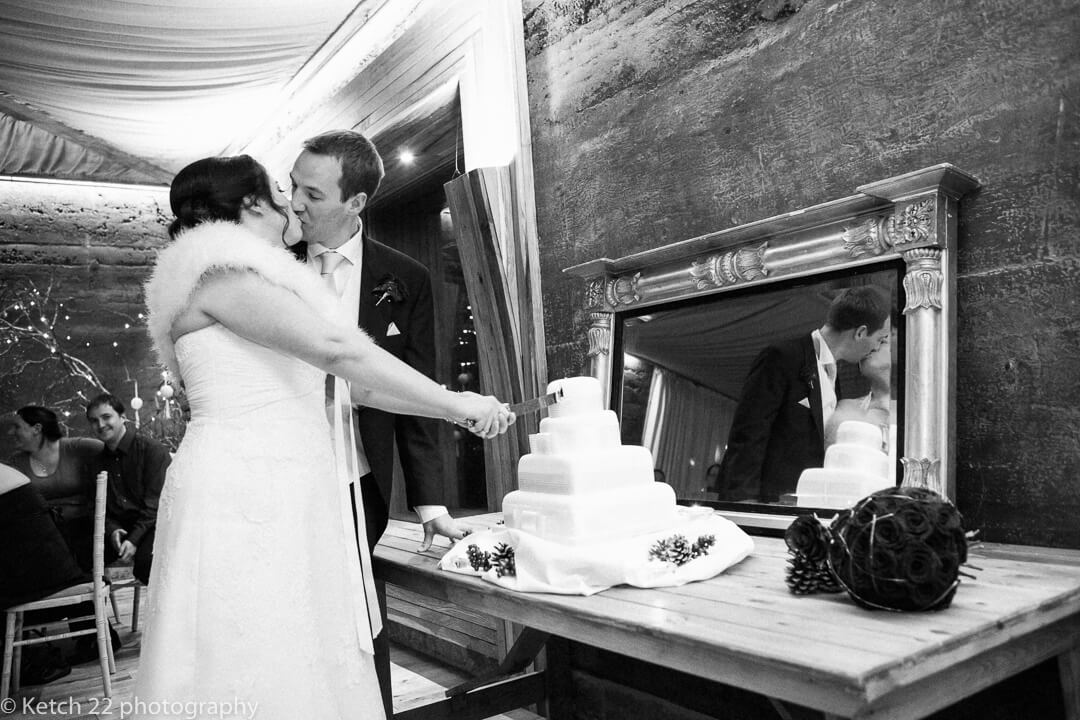 Bride and groom kissing whilst cutting the wedding cake