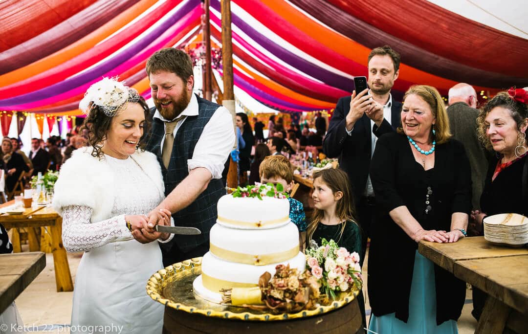 Bride and groom cutting cake with wedding guests looking on
