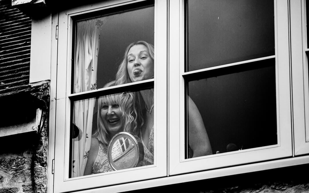 Bride and daughter looking through window and sticking out tongues