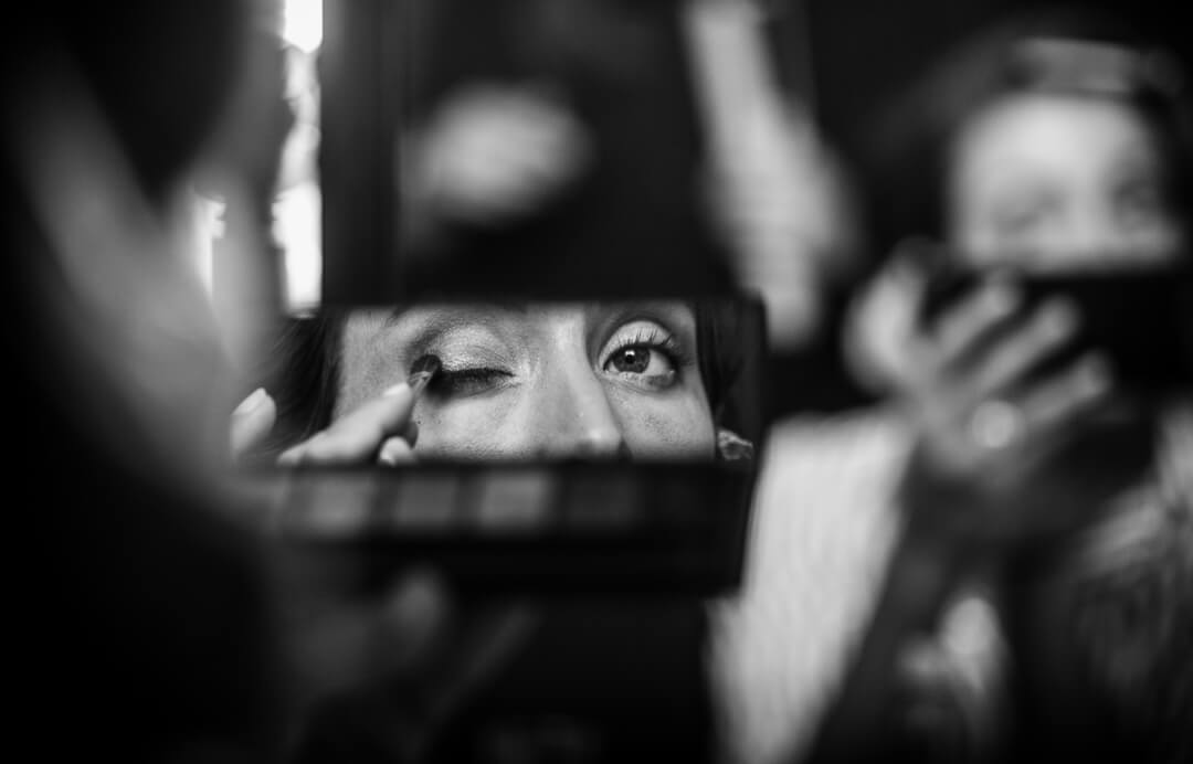 Bride applying make up whilst looking in mirror at preparations