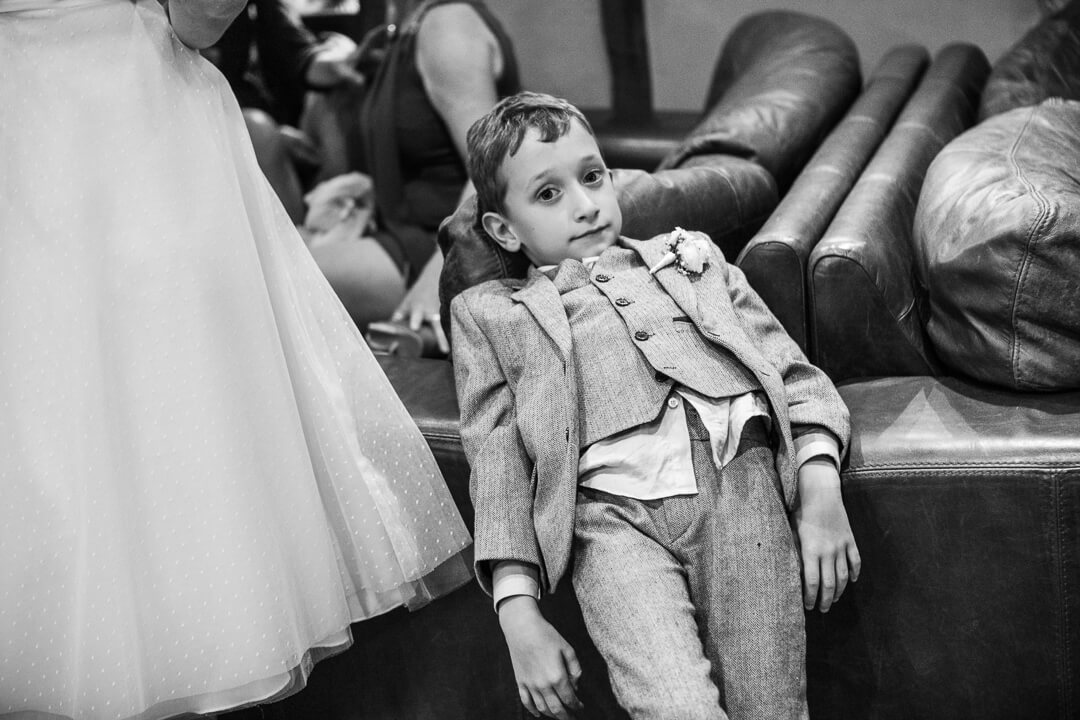 An example of a documentary weddings photo of a bored kid with his shirt hanging out at natural wedding
