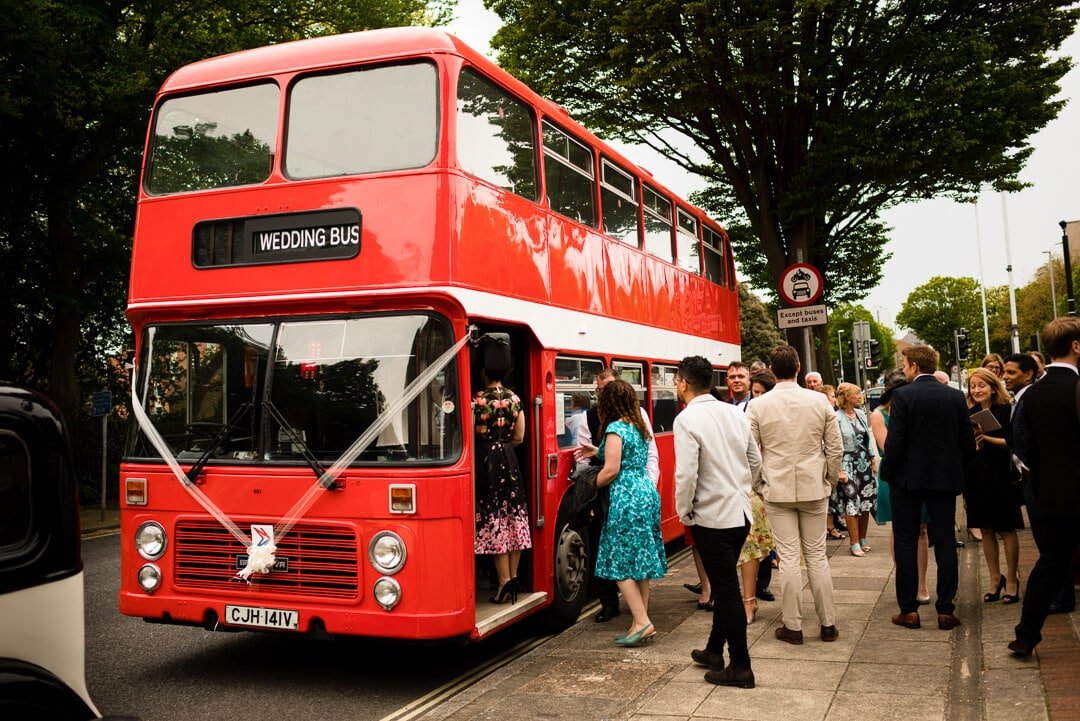 Wedding guests getting on red double decker bus