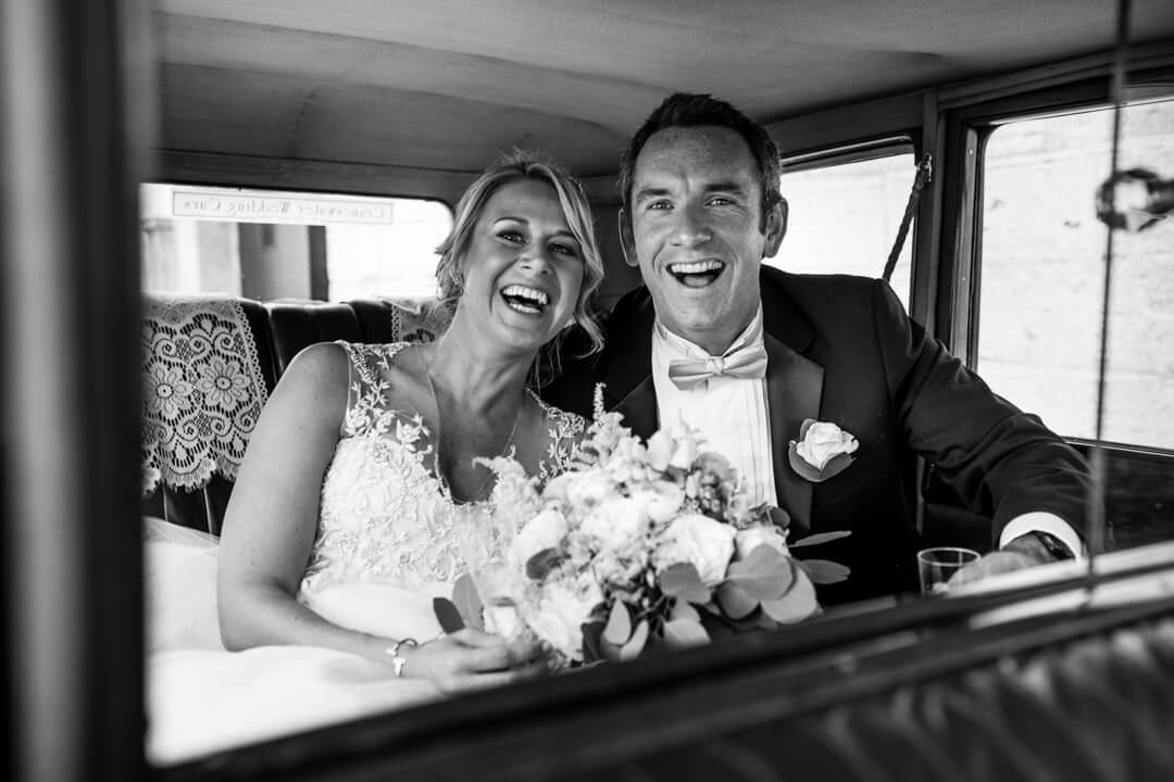 Bride and groom laughing in wedding car