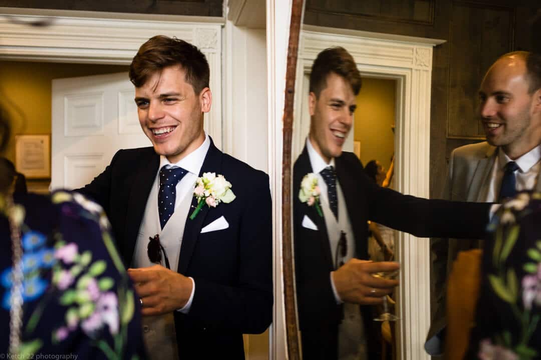 groom leaning against mirror at cheltenham wedding