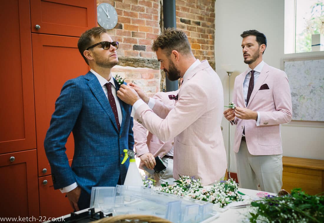 Groom with blue jacket being attended to by groomsmen with pink jackets