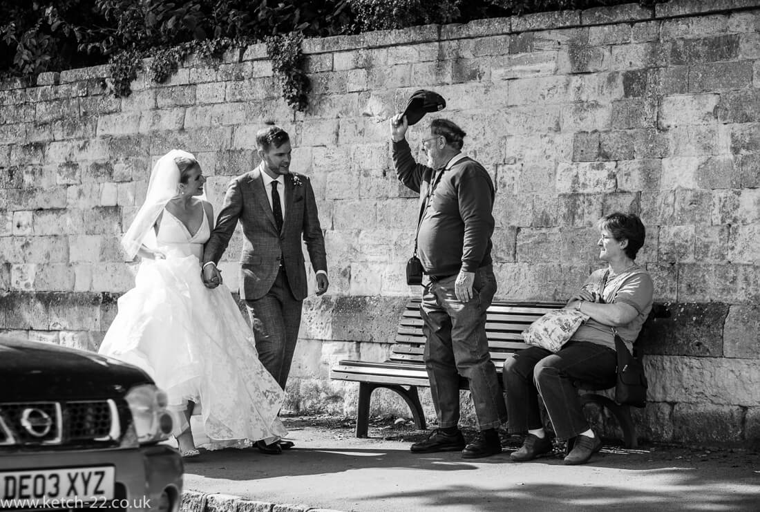 Member of public doffs his cap to bride and groom walking through Winchcombe