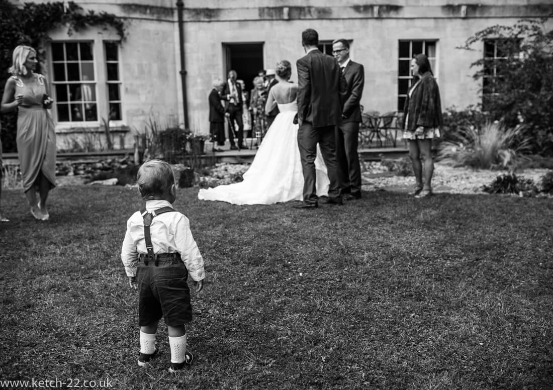 Page boy looks on as wedding guest arrive for drinks in garden