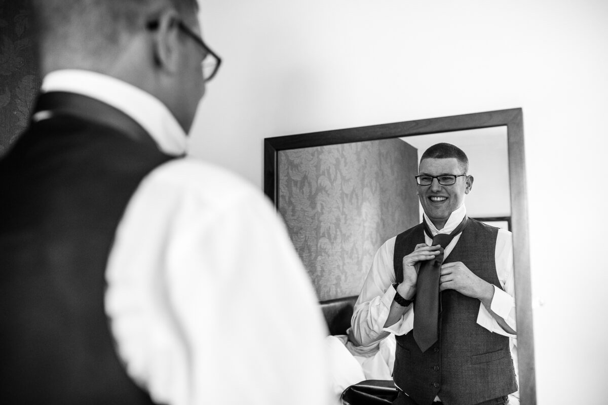 Groom putting on tie in mirror at Gloucestershire wedding