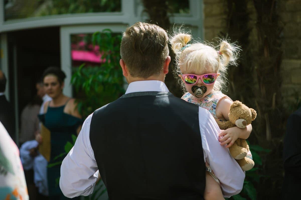 Little girl with blonde hair, pig tails and pink sunglasses at summer wedding