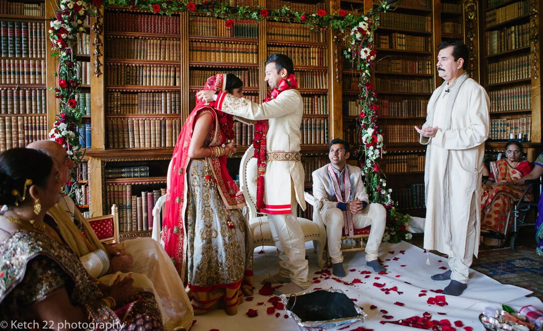 Groom puts flowers around neck of hindu bride at Highclere Castle wedding