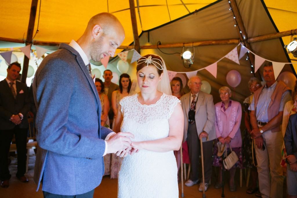 Bride and groom exchange rings at wedding ceremony in vintage marquee in Shropshire