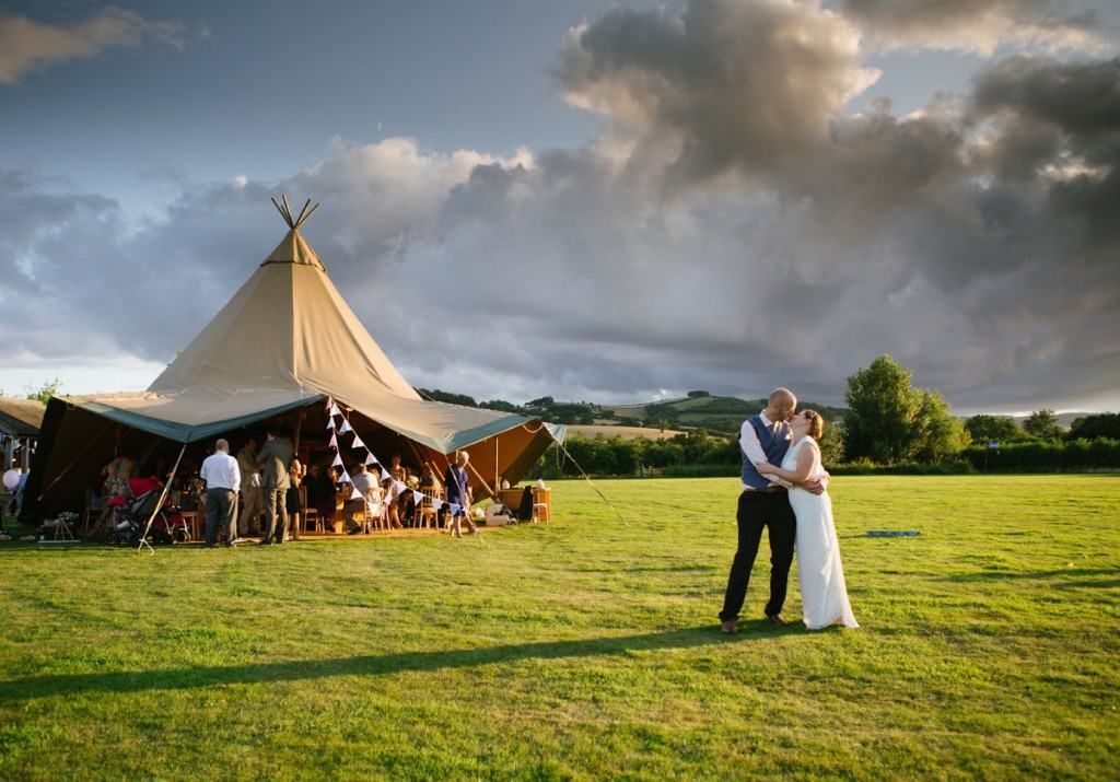Bride and groom kissing in front of wigwam tent at wedding in Shropshire