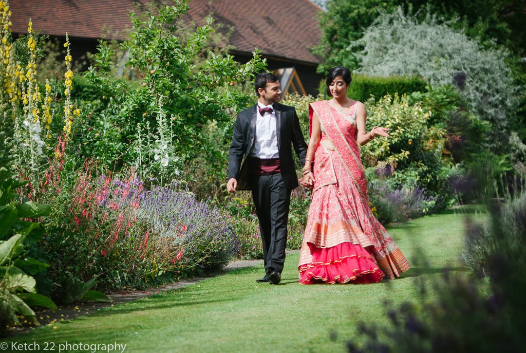 Hindu bride and groom walking through gardens at Micklefield Hall