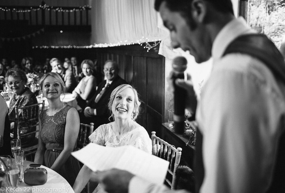 Bride smiling looking at groom whilst he makes wedding speech in Herefordshire