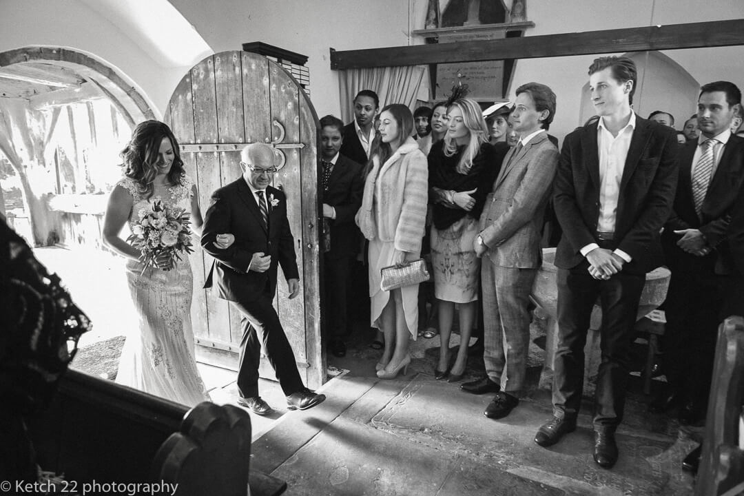 Father and bride enter church with wedding guests looking on in Herefordshire