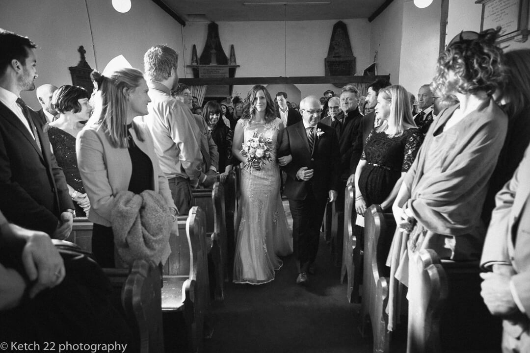 Reportage wedding photo of father and bride walking down church aisle