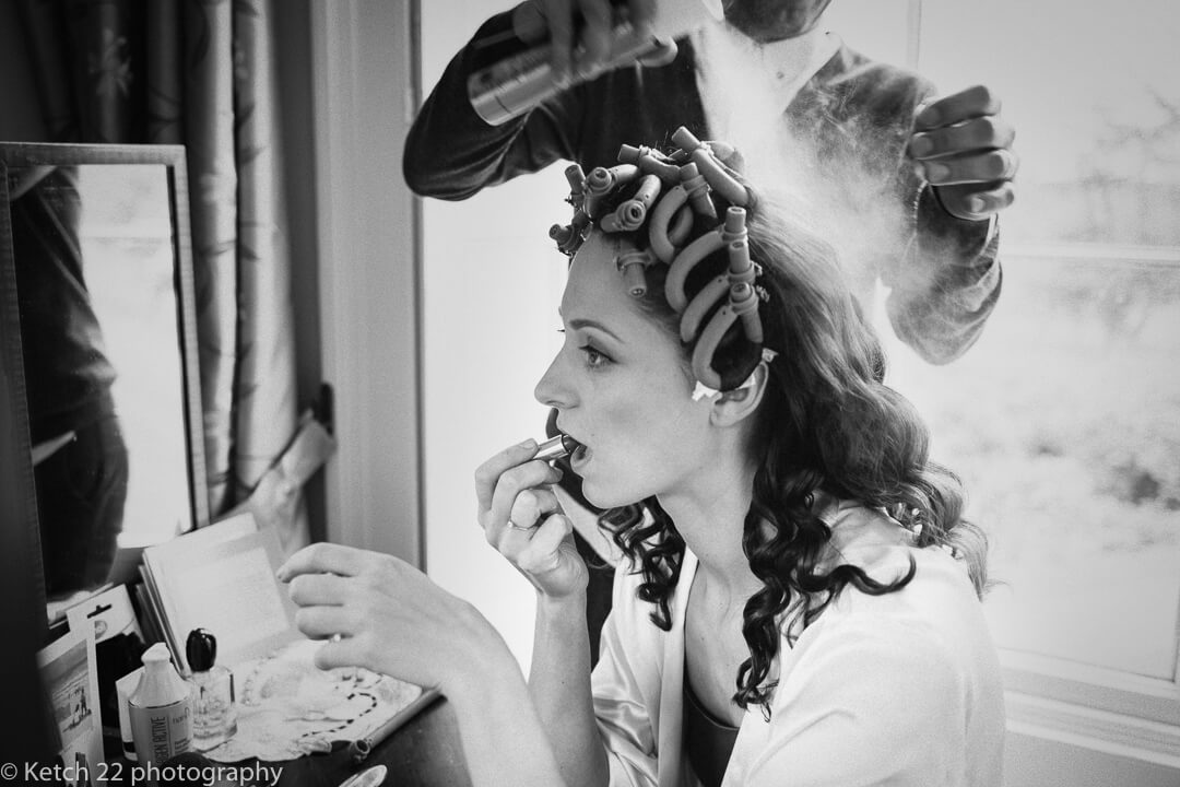 Bride having hairspray applied at wedding preparations 