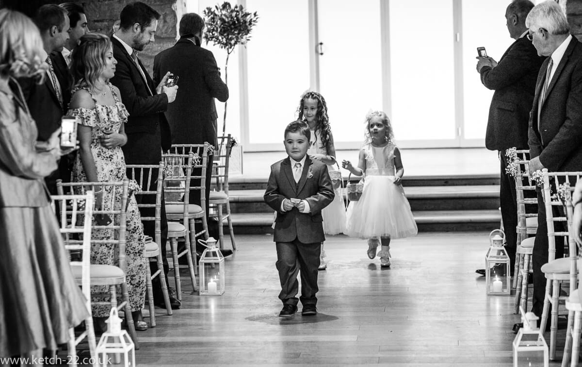 Page boy and flower girls enter wedding ceremony at The Great Tythe Barn in Gloucestershire