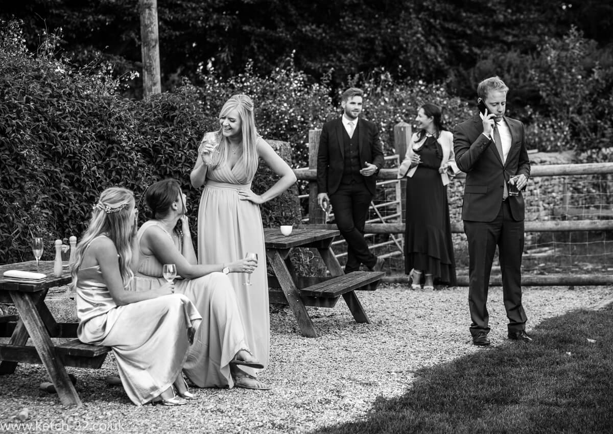 Bridesmaids chat on the lawn whilst wedding guest chats on the phone