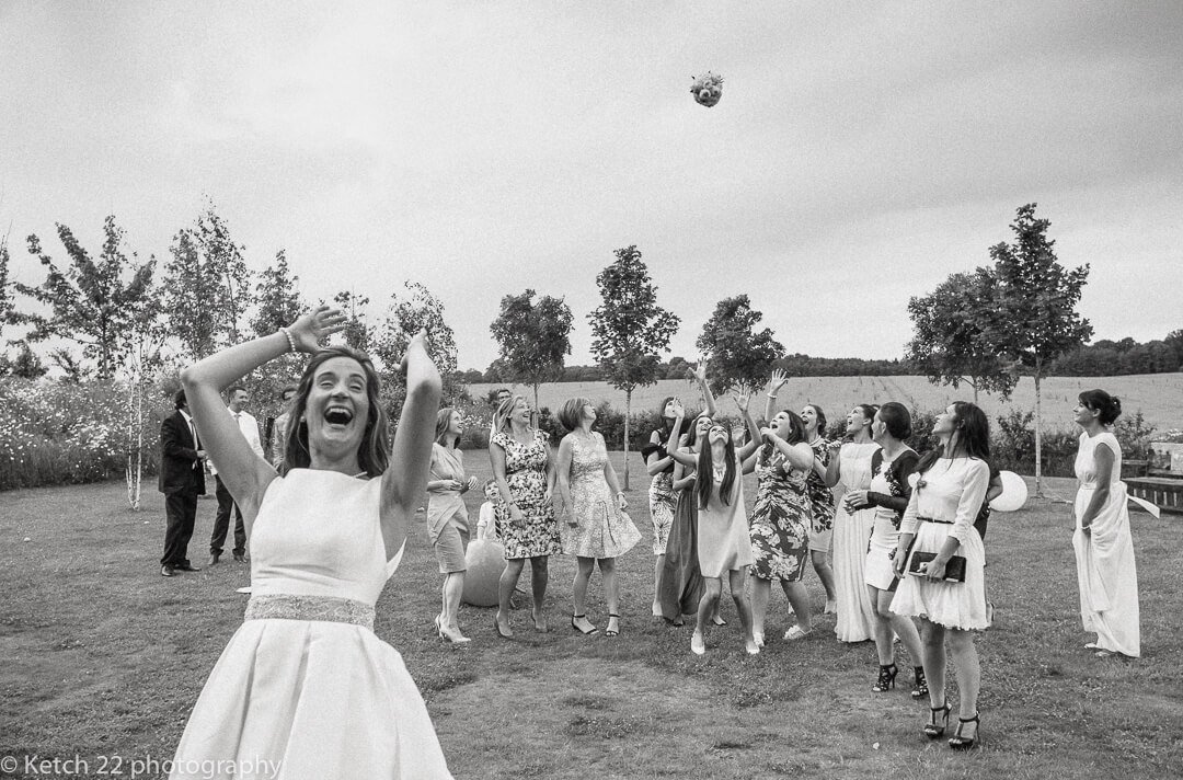 Bride throws bouquet of flowers while wedding guests try to catch it