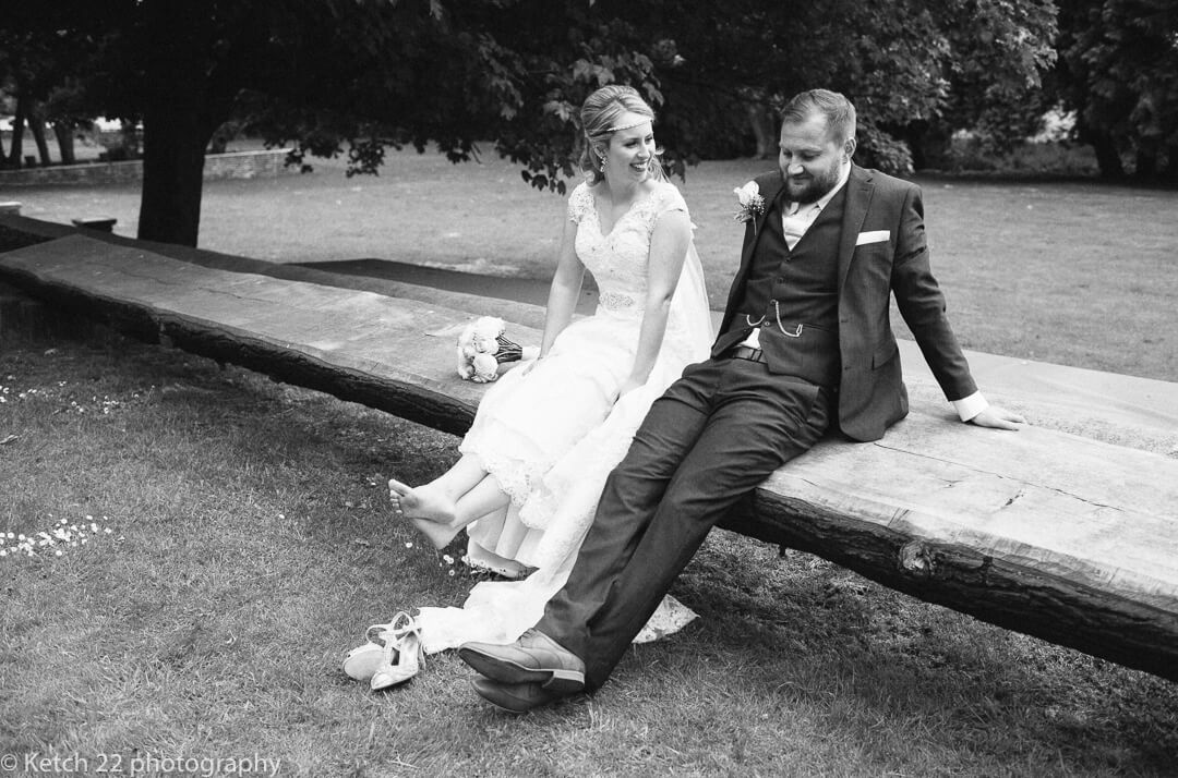 Bride with bare feet sitting on bench with groom at eastington House wedding