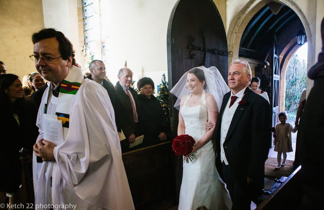 Father and bride entering church with wedding guests looking on