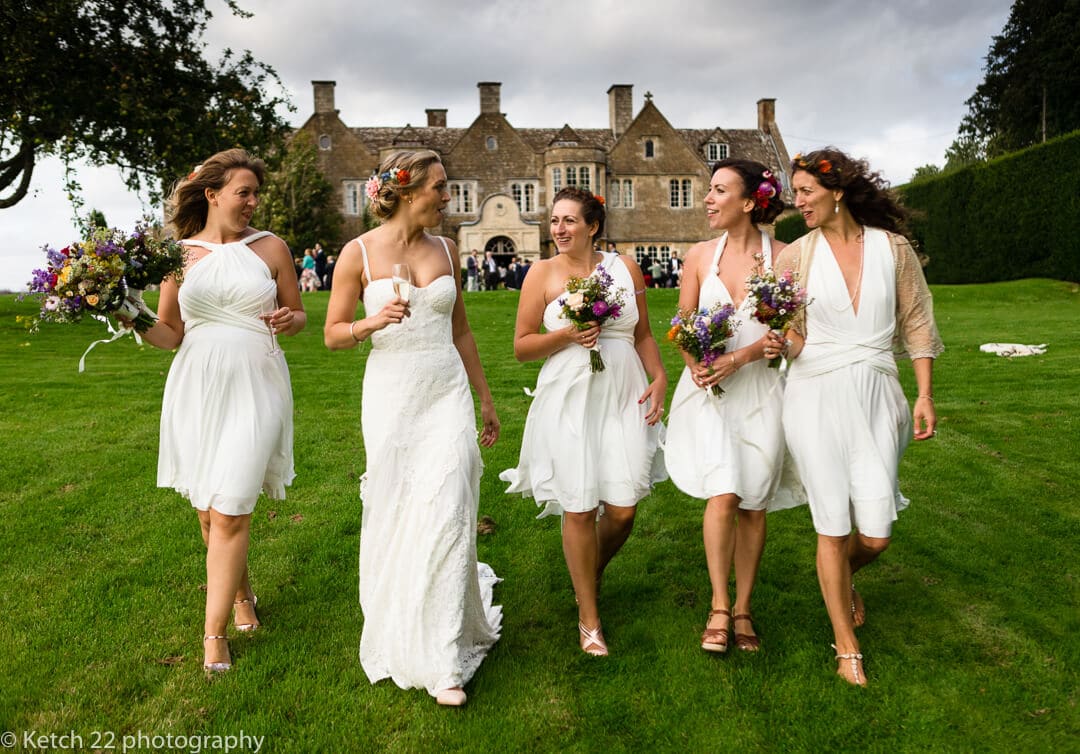 Bride and bridesmaids walking and laughing in front of Hilles House in Gloucestershire
