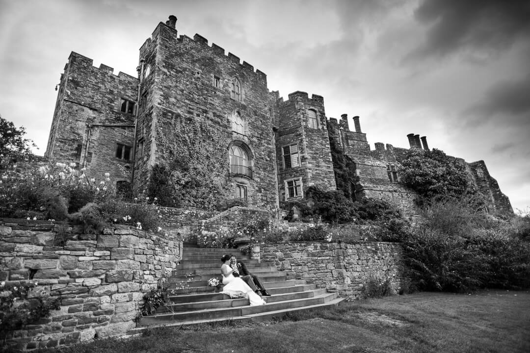 Bride and groom sat on steps in front of Berkeley Castle wedding venue