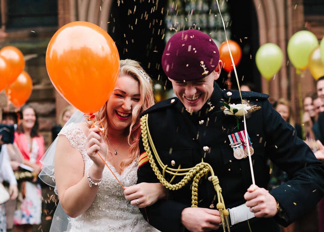 Bride with orange balloon and groom with purple army beret get showered with confetti