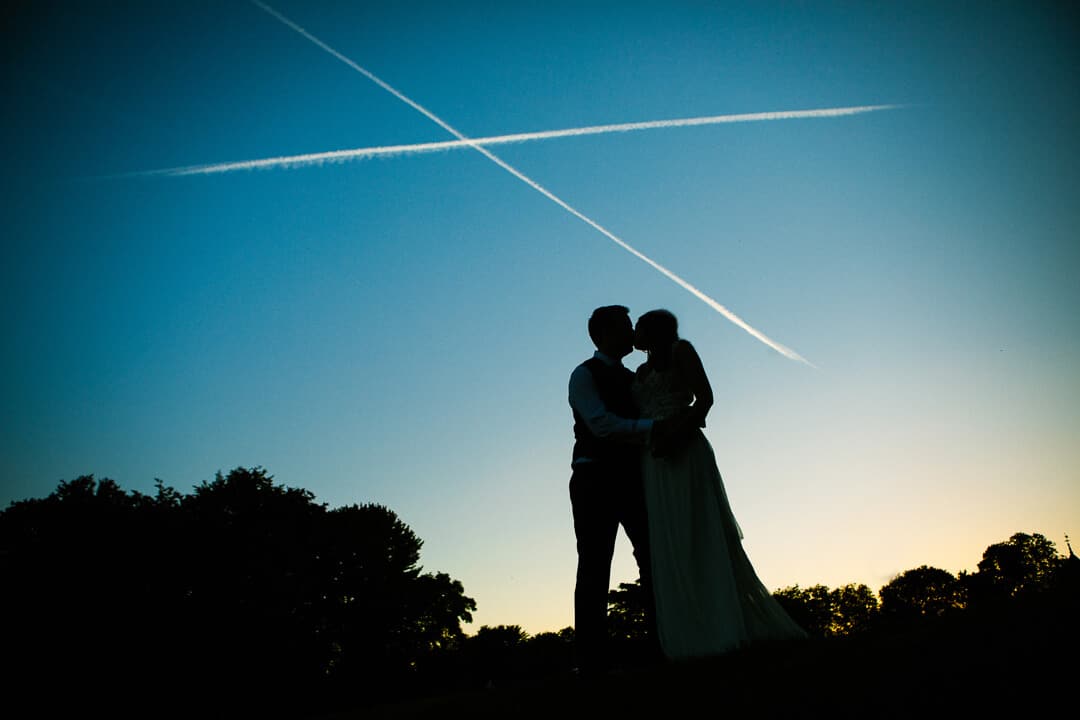 Silhouette of bride and groom kissing at sunset at summer wedding
