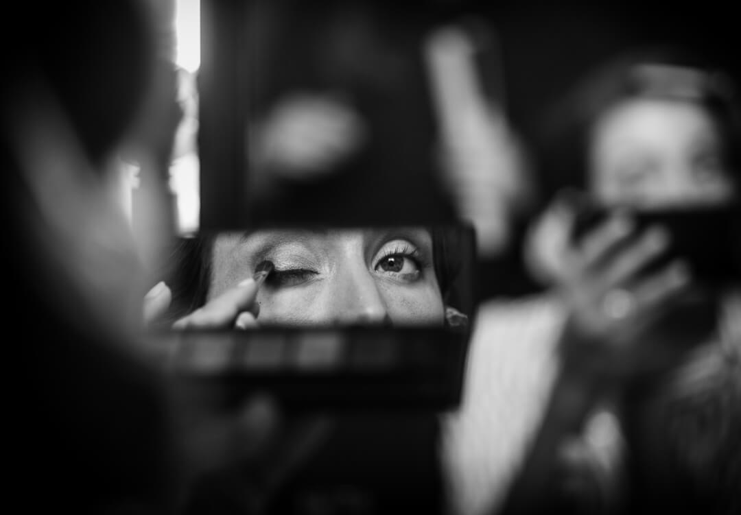 Bride looking in mirror putting on make up at wedding preparations