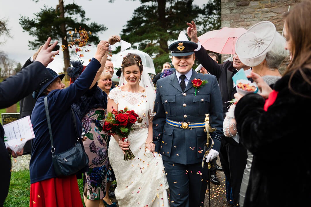 Bride with red roses and groom in RAF uniform walking through confetti