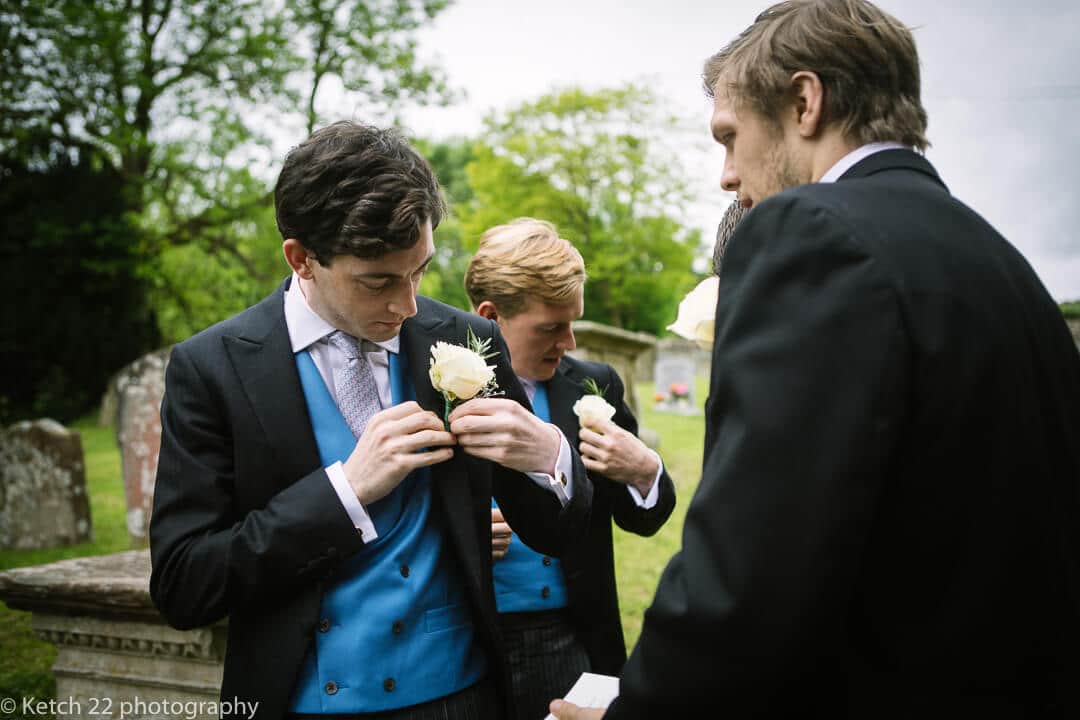 Groom with blue waistcoat putting on yellow rose at documentary wedding in Oxfordshire