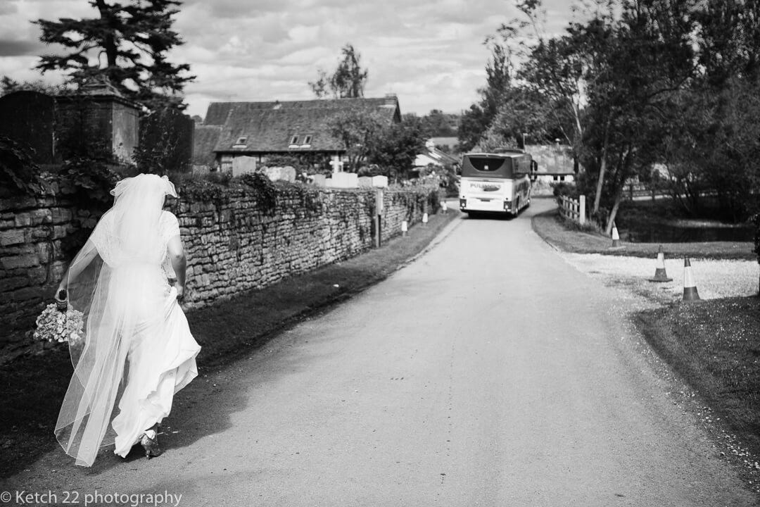 Bride walking down country lane as wedding bus leaves