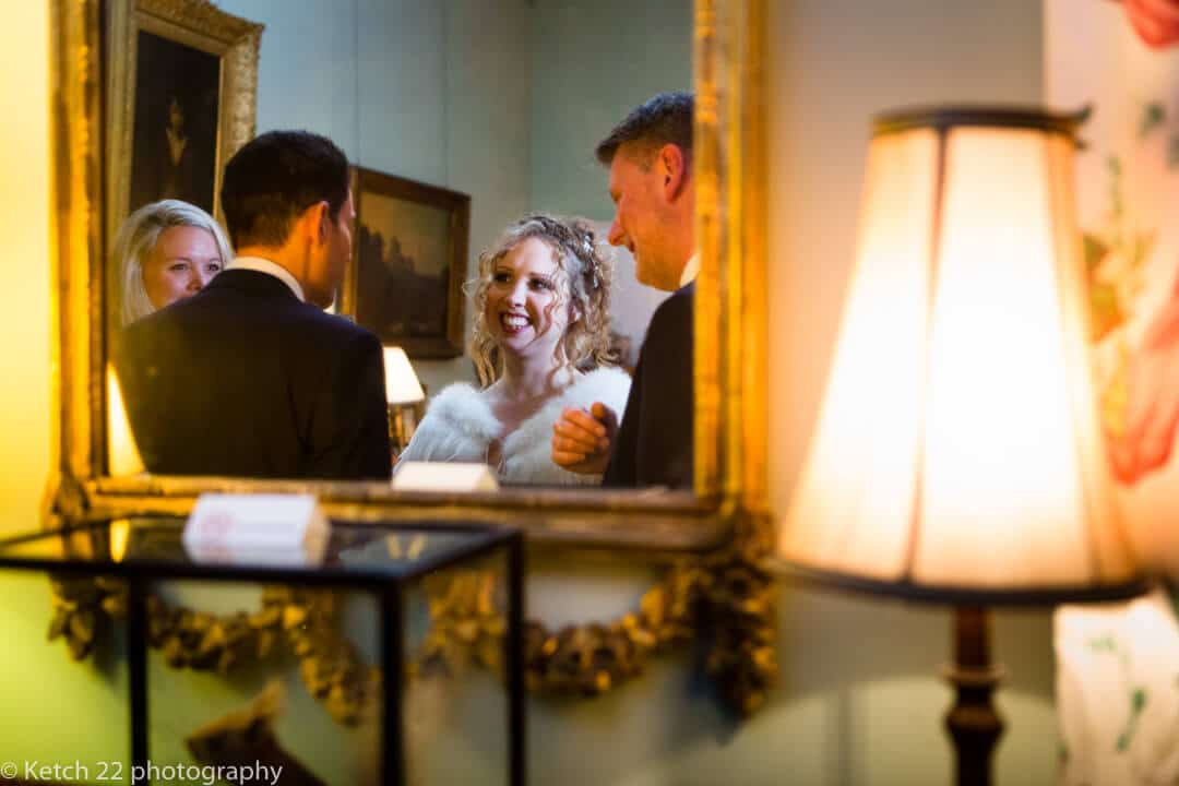 Natural portrait of bride in mirror chatting to wedding guests