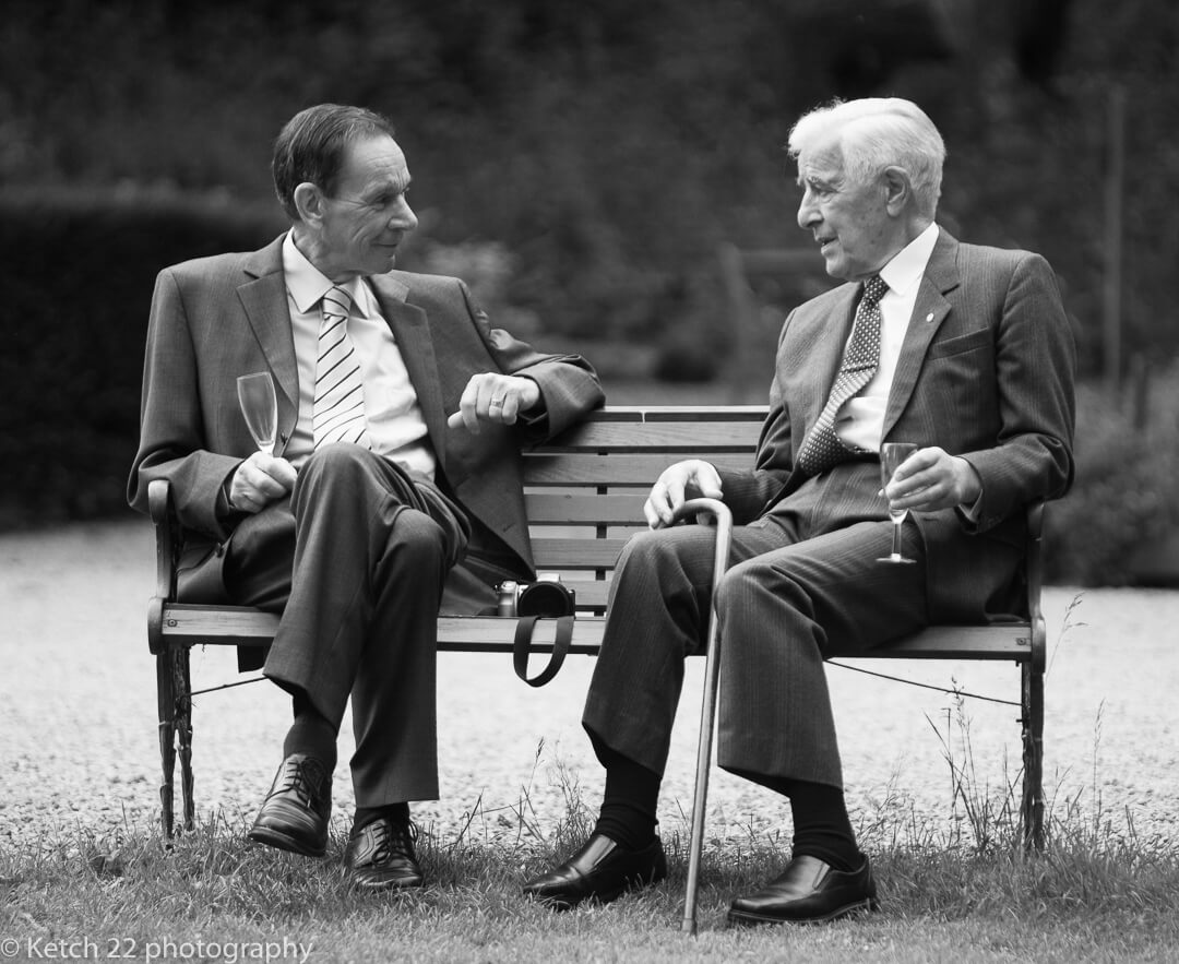 Two grandads sat on bench talking at wedding reception