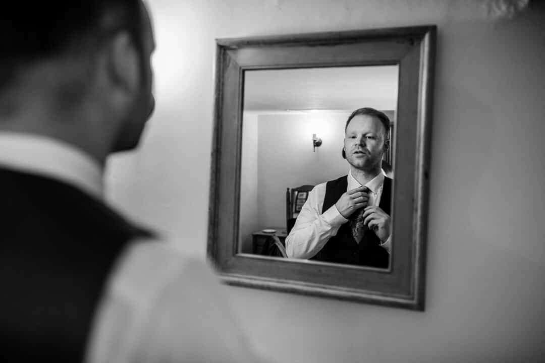 Groom putting on tie in mirror at wedding