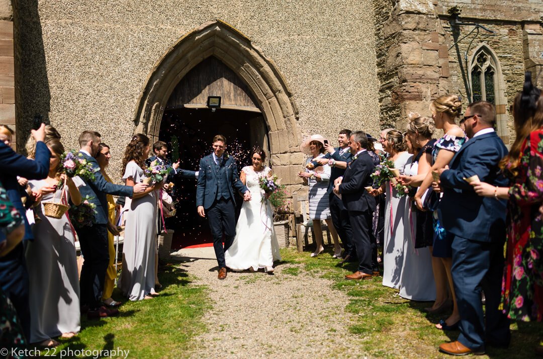 Bride and groom leaving church and getting showered with confetti