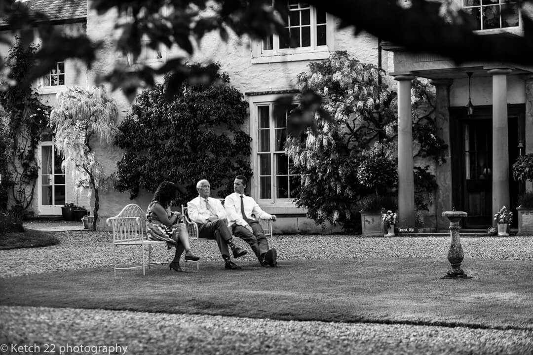 Wedding guests chat on bench in garden