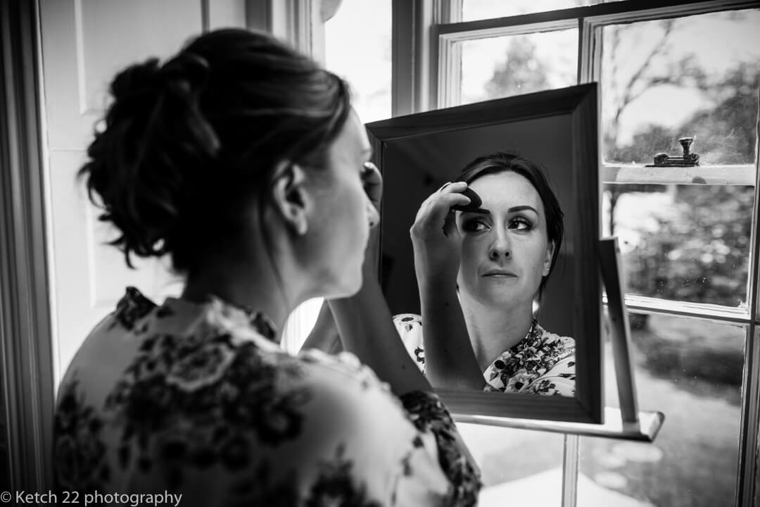 Bride looking in mirror and putting on makeup at wedding